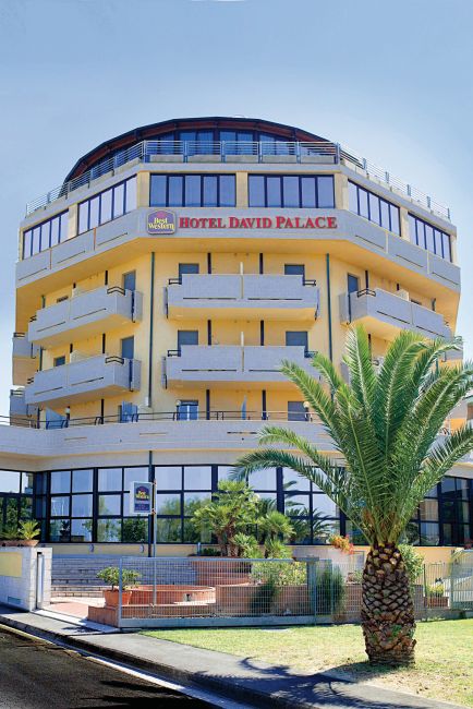 Facciata di hotel giallo con palme e balconi.