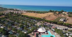 Vista aerea di un villaggio con piscina e campo coltivato vicino alla costa.