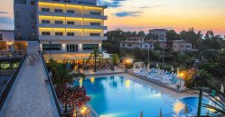 Piscina illuminata al tramonto davanti a un hotel.