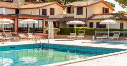 Piccola piscina con lettini e ombrelloni vicino a edifici residenziali.