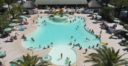 Piscina affollata con giochi d'acqua, palme e lettini circostanti.