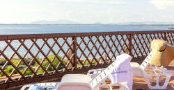 Lettini e cappello di paglia su una terrazza con vista mare e montagne all'orizzonte.