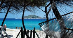Vista sul mare azzurro, amaca e alberi in primo piano, piccola isola in lontananza.