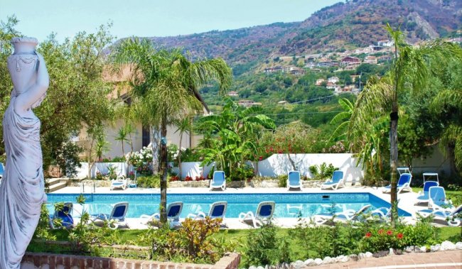 Giardino con piscina, statue e lettini blu.