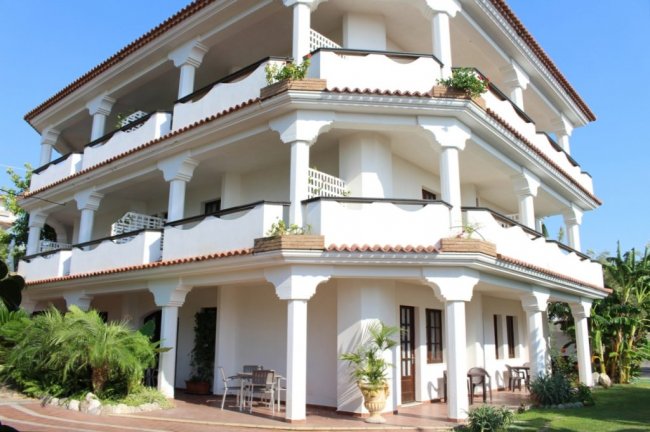 Edificio bianco a tre piani con balconi e piante.