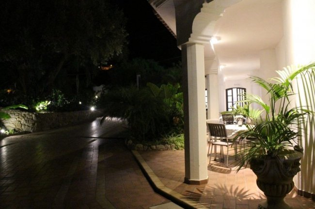 Portico esterno illuminato di notte con piante e tavolo.