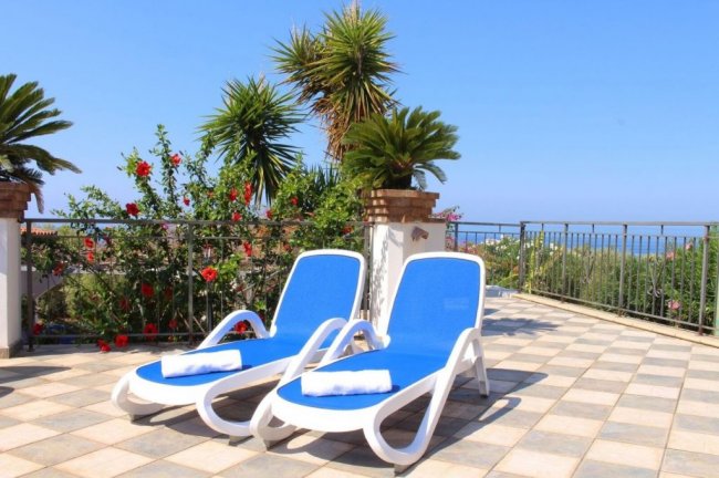 Due sdraio blu su terrazza con vista giardino e mare.