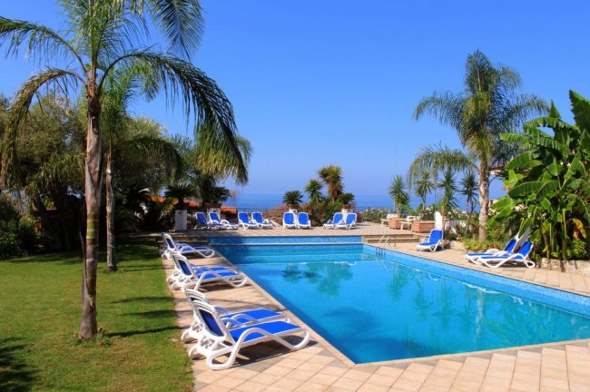 Piscina con lettini e palme, sotto un cielo blu.