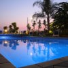 Piscina illuminata al tramonto con palme e cielo viola.
