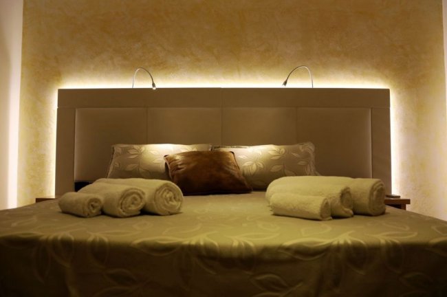 Un letto con testiera illuminata e asciugamani arrotolati.