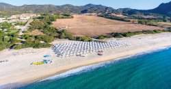Lunga spiaggia di sabbia con file di ombrelloni bianchi, mare azzurro e colline sullo sfondo.