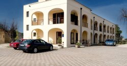 Edificio a due piani con archi e balconi, auto parcheggiate davanti.