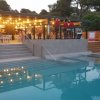 Piscina con bar illuminato e tavoli all'aperto.