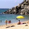 Spiaggia con persone in acqua e ombrellone giallo.