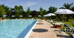 Piscina all'aperto con lettini e ombrelloni bianchi su una terrazza.