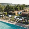 Piscina all'aperto con sdraio e ombrelloni, vista di colline e bungalow in lontananza.