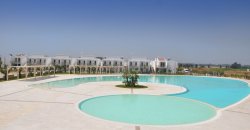 Ampia piscina a forma irregolare con edifici bianchi sullo sfondo.