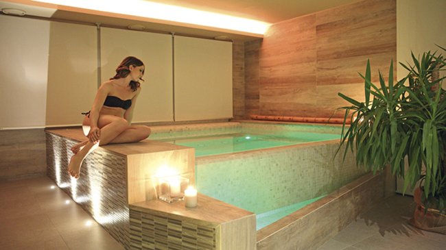 Donna in costume da bagno seduta su un bordo piscina moderna e luminosa.