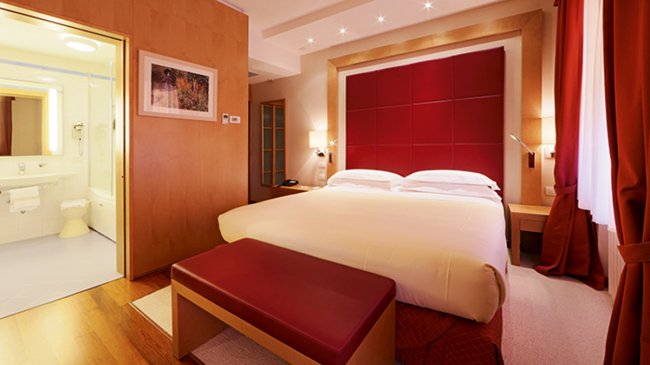 Camera d'albergo elegante con letto matrimoniale e colori rossi.