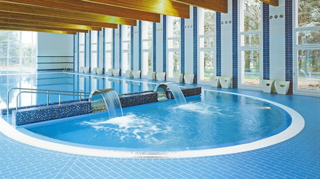 Piscina interna con cascate d'acqua e grandi finestre.