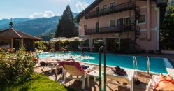 Piscina, sdraio e edificio rosa, con montagne sullo sfondo.