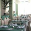 Sala da pranzo con tavoli apparecchiati, tovaglie verdi e piante decorative.