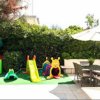 Area giochi per bambini all'aperto con scivolo, casetta e tavolino vicino a un tavolo esterno.