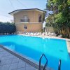 Piscina azzurra all'aperto con lettini bianchi e una casa sullo sfondo.