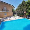 Vista della piscina circondata da lettini bianchi e alberi rigogliosi.