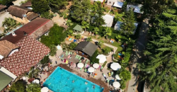 Piscina all'aperto circondata da alberi e persone che prendono il sole.