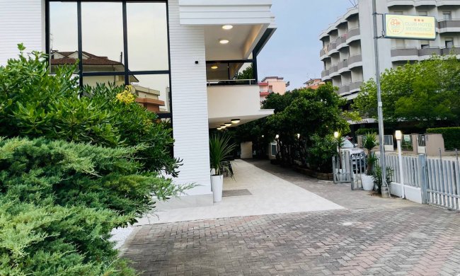 Edificio bianco con vetrate, piante lungo il vialetto.