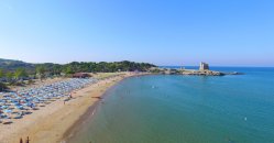 Spiaggia con lettini e ombrelloni lungo la costa, acqua calma e una torre in lontananza.