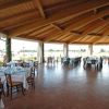 Un ampio spazio esterno coperto con tavoli apparecchiati, vista su giardino e tetto in legno.