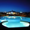 Una piscina illuminata di notte davanti a un edificio con luci accese, cielo blu scuro sullo sfondo.