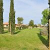 Un prato verde con cipressi e alberi, circondato da edifici con tetti rossi.