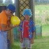 Un uomo gonfia un palloncino vicino a un bambino con una parrucca blu in un giardino.