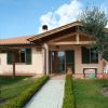 Casa con portico in legno, persiane verdi e giardino curato con siepe e alberi.