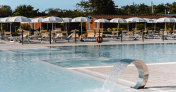 Piscina con getto d'acqua, circondata da lettini e ombrelloni bianchi.