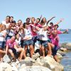 Gruppo di persone sorridenti su rocce vicino al mare.