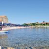 Spiaggia con mare cristallino, ombrelloni e un vecchio edificio in pietra.