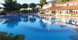 Grande piscina circondata da edifici e ombrelloni.