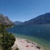 Spiaggia di ciottoli con persone, immersa tra montagne e lago.