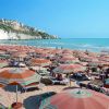 Una spiaggia affollata con ombrelloni arancioni e vista di scogliere sullo sfondo.