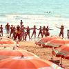 Persone partecipano a un'attività di gruppo sulla spiaggia, con ombrelloni colorati in primo piano.