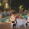 Persone sedute a tavoli attorno a una piscina con fontana, di sera.