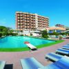 Piscina all'aperto con sdraio e ombrelloni blu, edificio sullo sfondo sotto un cielo azzurro.