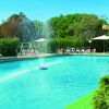 Piscina con fontana centrale, circondata da vegetazione e lettini bianchi sotto ombrelloni.