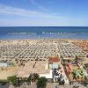Spiaggia affollata con file di ombrelloni e mare sullo sfondo.