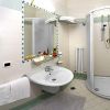 Bagno con doccia angolare, lavabo, specchio e asciugacapelli a parete.