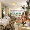 Sala da pranzo elegante con tavoli apparecchiati, piante decorative e buffet di cibo e vino.